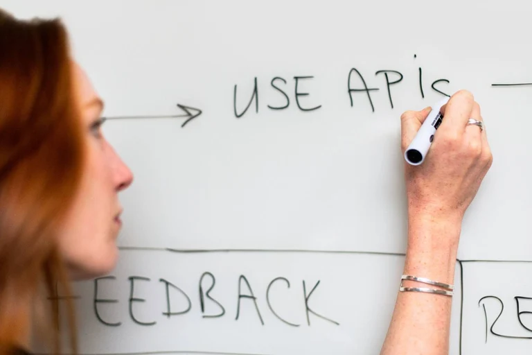 A software engineer is writing the text 'Use APIs' on a whiteboard in a technical diagram.