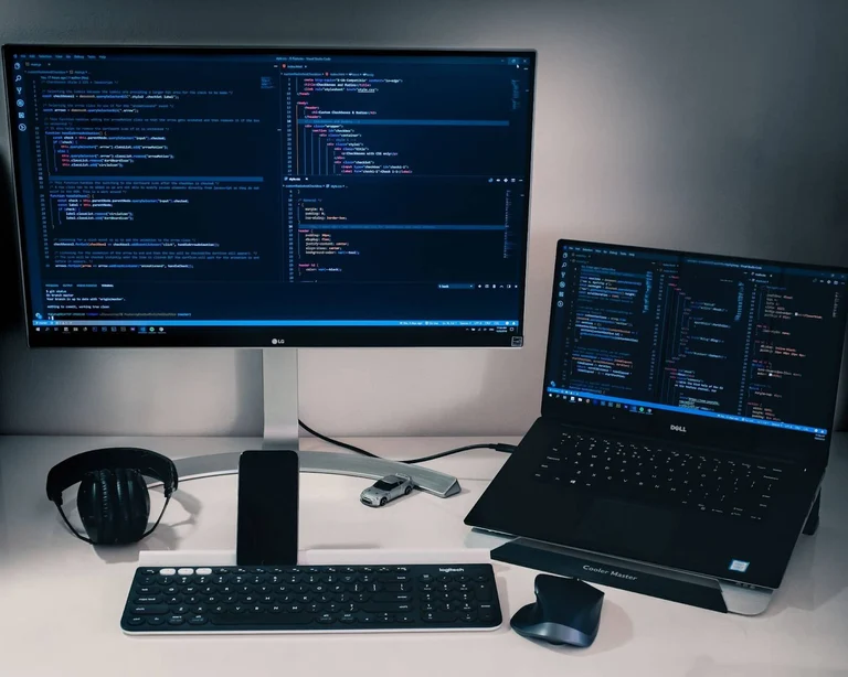 Two computers sitting side-by-side with coding appearing onscreen. 