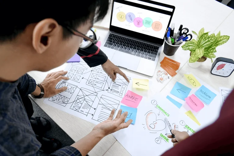 An image of a man planning the user research phase of a project. He's looking at different sheets that outlined the process with stages like empathize, define and ideate. 