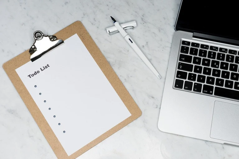 Picture showing a MacBook laptop on the right, a pen in the middle, and an empty To Do list on a sheet of paper in the left 