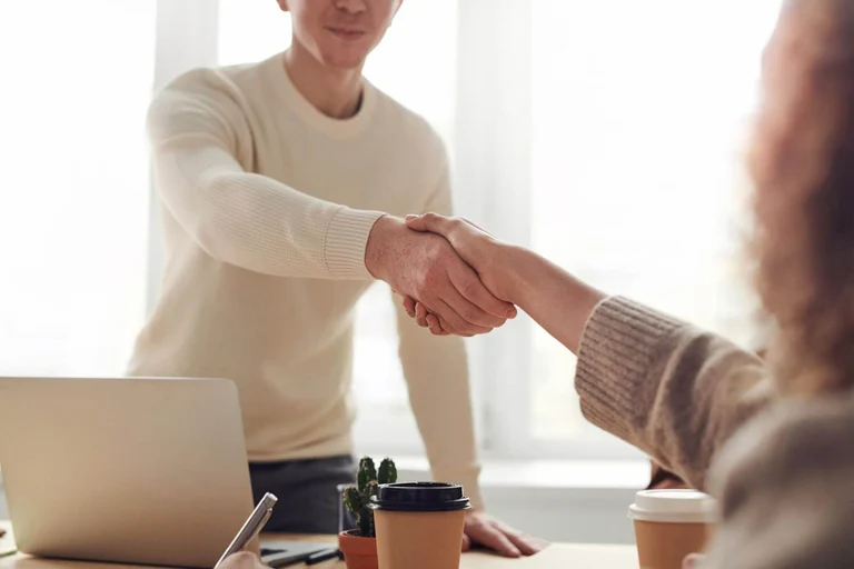 A recruiter is pictured shaking the hands of an applicant.