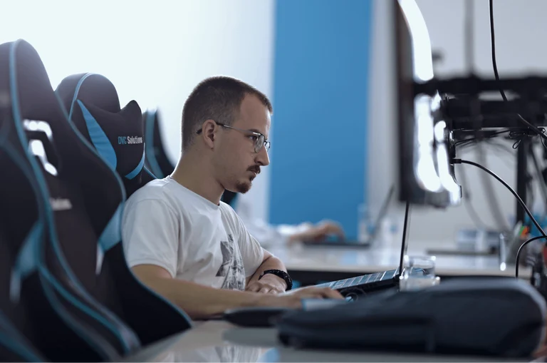 Employee is seen from the side working on a computer in a white t-shirt and glasses