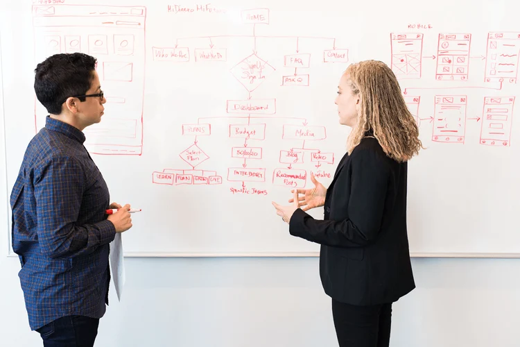Two people discuss frameworks in front of a whiteboard. 
