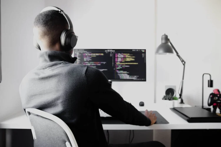 A make ERP developer wearing headphones and looking at a computer monitor filled with lines of code. 