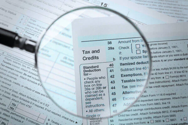 A magnifying glass hovers over a tax form, magnifying the print. 