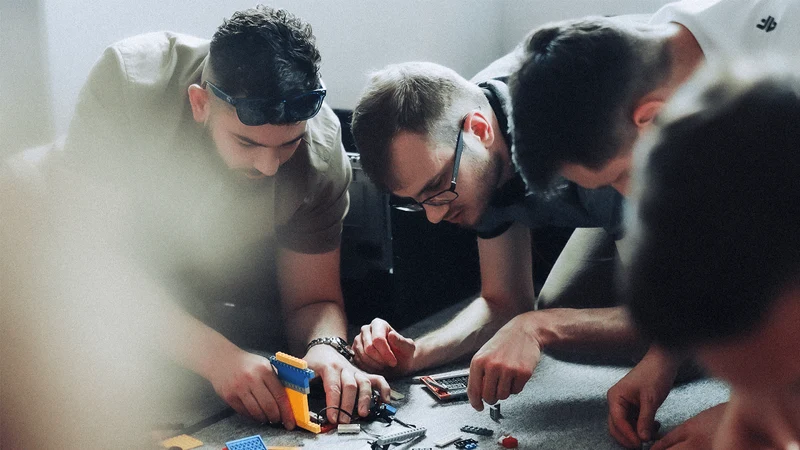 Four developers sit on the floor, leaning in and tinkering with pieces of Lego and wires to visualize solutions. 