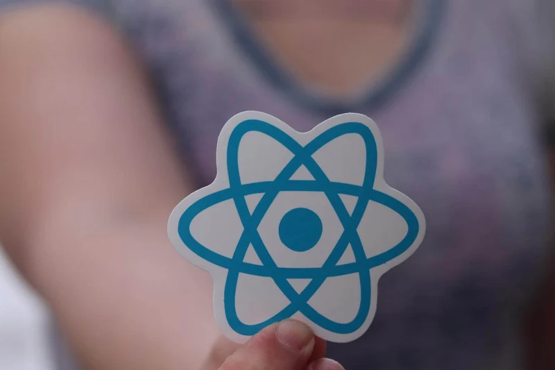 The image contains a hand holding a ReactJS sticker.
