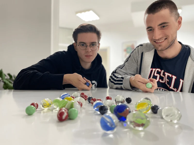 Two employees are playing marbles on a table with an assortment of colorful marbles.