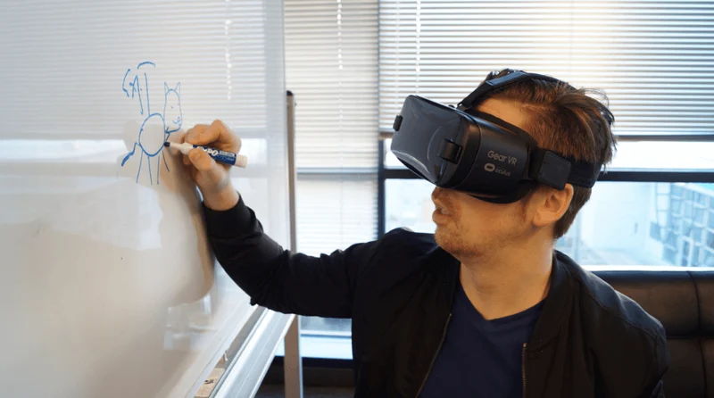 Man wearing a VR headset and writing on a whiteboard with a blue marker.