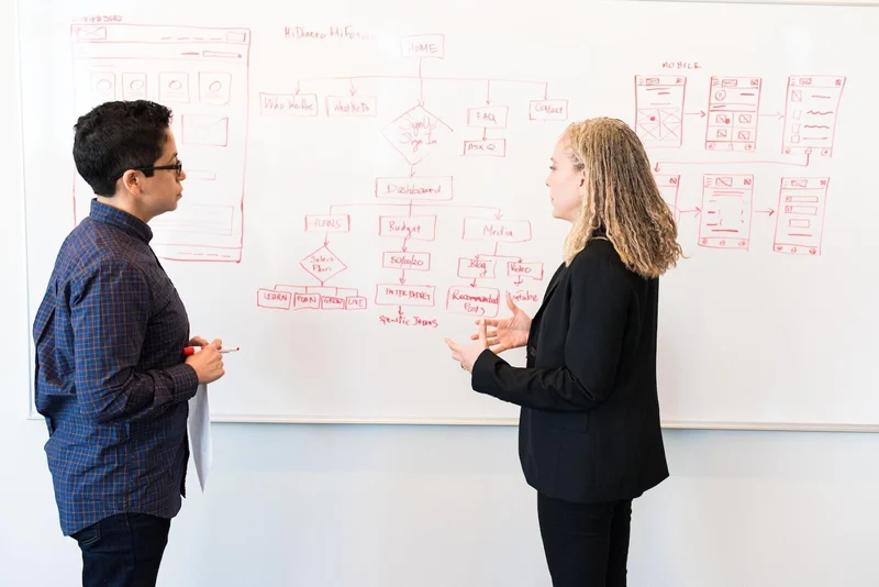 Two team members drawing a technical diagram of application design and architecture at a whiteboard