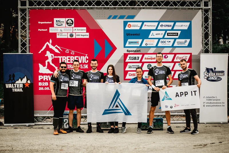 7 team members are holding up APP IT banners at an outdoor fitness event