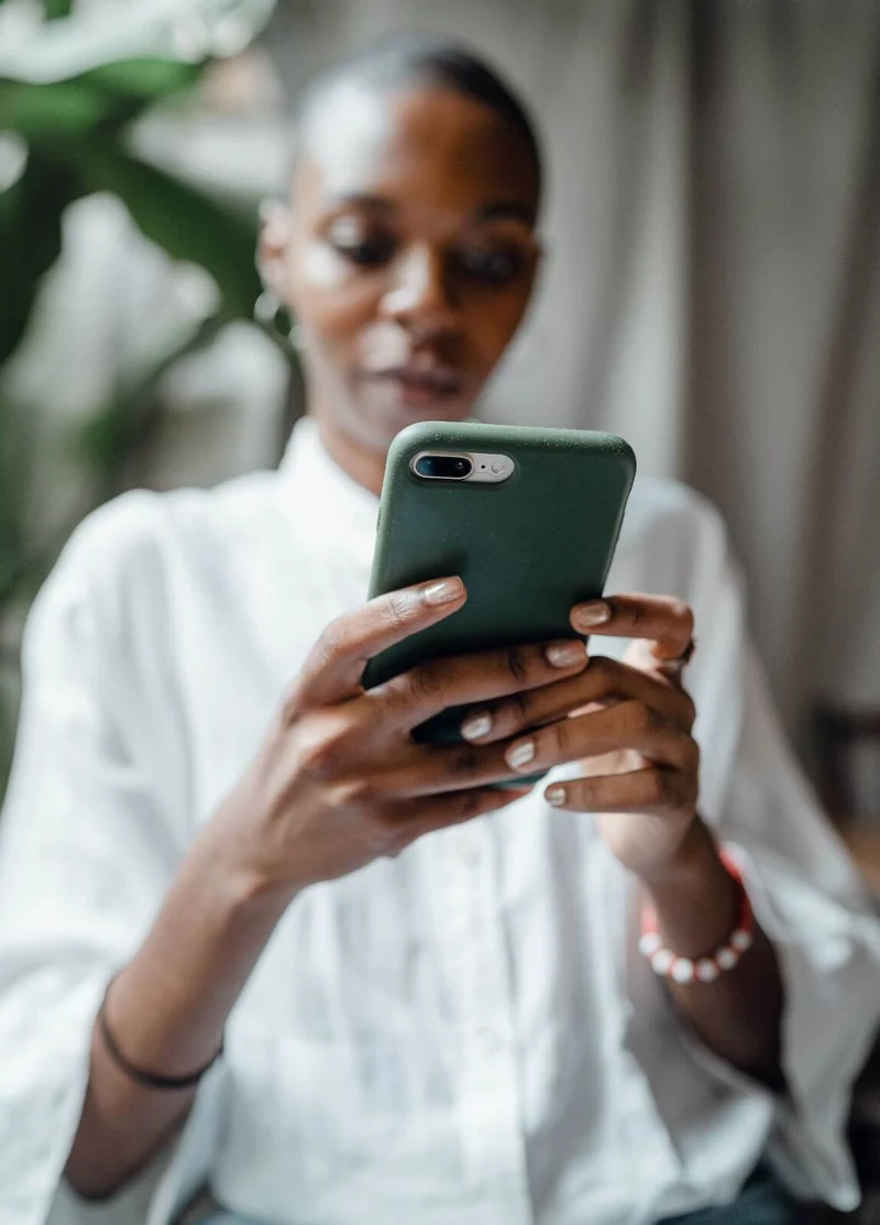 A bald Black woman wearing a white collared shirt and gold hoop earrings checks the reviews for an app development agency on her smartphone.