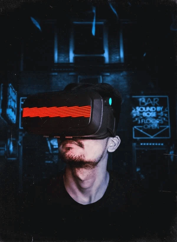 A man looking to the left wears a black VR headset with red neon across the eyes.